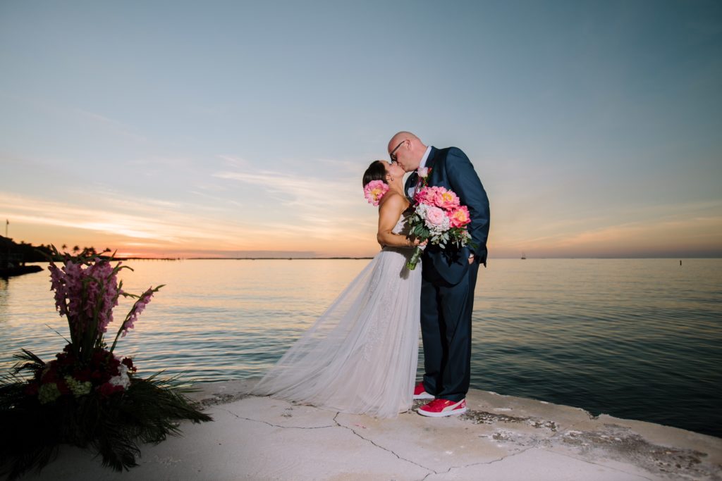 Bride and groom kissing at sunset overlooking ocean